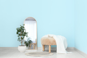 Floor mirror, pouf and houseplant near blue wall in interior of room