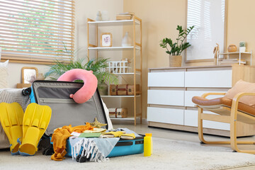 Packed suitcase with clothes and beach accessories on carpet in room