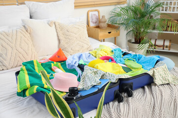 Packed suitcase with clothes and beach accessories on bed in bedroom, closeup
