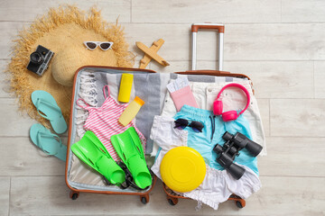 Open suitcase with clothes, binoculars and accessories on floor in room