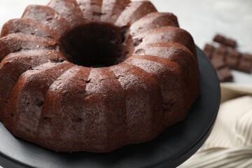 Tasty bundt cake and pieces of chocolate on table, closeup