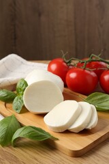 Tasty mozzarella, tomatoes and basil on wooden table, closeup