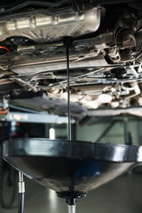 Dirty old motor oil dripping from car engine into container in workshop, closeup