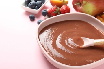 Baby food. Eating tasty puree with spoon at pink table, closeup. Space for text
