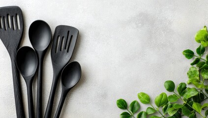 Black kitchen utensils on gray surface with greenery.  Useful for cookbooks