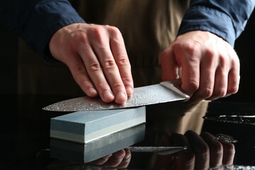 Man sharpening knife with sharpener at mirror table, closeup