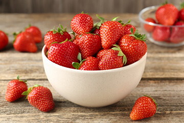 Fresh ripe strawberries in bowl on wooden table, closeup