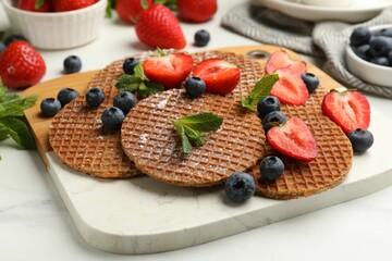 Tasty Dutch waffles (stroopwafels), mint and strawberries on white marble table, closeup