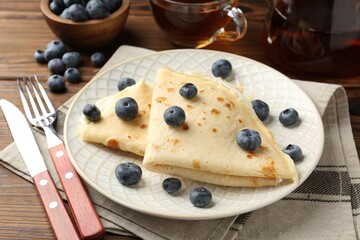Tasty crepes with blueberries and tea served on wooden table, closeup