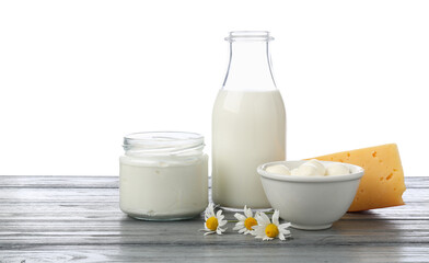 Different fresh dairy products and chamomile flowers on grey wooden table against white background