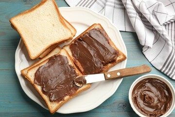 Tasty chocolate butter in bowl, slices of bread and knife on light blue wooden table, flat lay