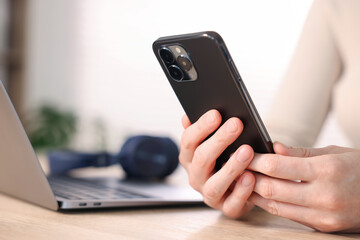 Woman using modern smartphone at wooden table indoors, closeup