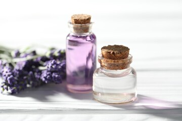 Natural essential oil and lavender flowers on white wooden table, closeup