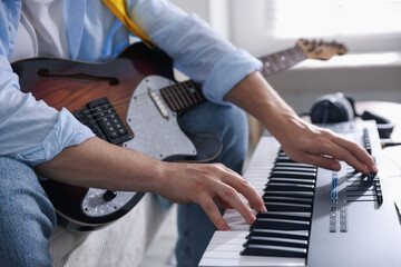 Man working with MIDI keyboard and guitar indoors, closeup