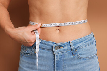 Woman measuring waist circumference on beige background, closeup