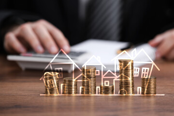 Increase in real estate value. Stacked coins with illustration of houses. Man working at table,...
