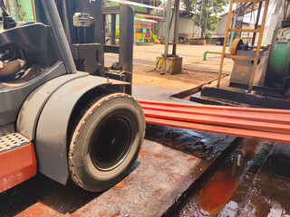 Forklift moving red metal bars at industrial site under bright daylight condition. Close-up of a...