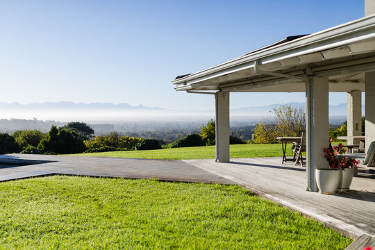 Backyard patio roof is shading wooden deck with pillars, table, chairs, planters, and valley view