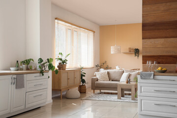 Interior of stylish room with beige sofa, table, chest of drawers and white counters