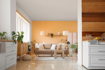 Interior of stylish room with beige sofa, table, chest of drawers and white counters