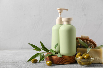 Bottles of cosmetic products with olives on white grunge background, closeup