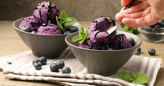 Woman eating tasty sorbet with blueberries and mint at wooden table, closeup