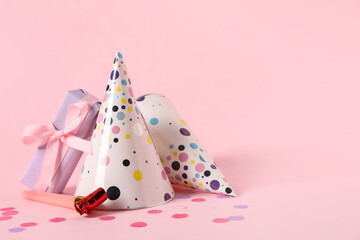 Composition with party hats, gift box and whistles on pink background, closeup