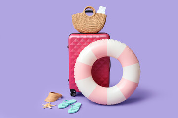 Suitcase, inflatable ring and beach accessories on lilac background
