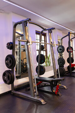 Smith machine bench press station occupying gym corner, with weight plates and mirrored walls