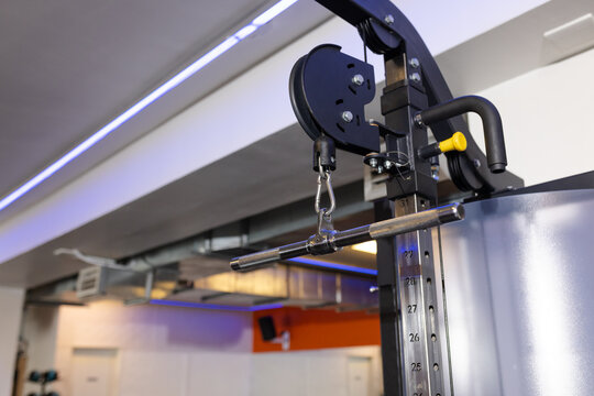 Cable pulley wheel and metal carabiner attaching steel cable to lat pulldown bar in gym