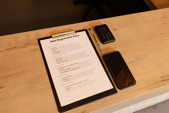 Black clipboard holding gym registration form lying on countertop with smartphone and card reader