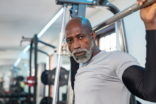 African American man lifting barbell on Smith machine in gym weight area wearing compression shirt
