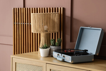 Houseplants, record player and lamp on chest of drawers near brown wall in living room, closeup