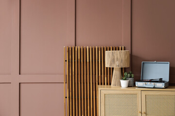 Chest of drawers with record player and folding screen near brown wall in living room, closeup