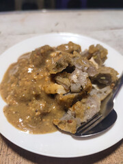 Indonesian Batagor with peanut sauce served on a white plate with a metal fork. Traditional Indonesian batagor dish with rich peanut sauce, served on a white plate with a fork.