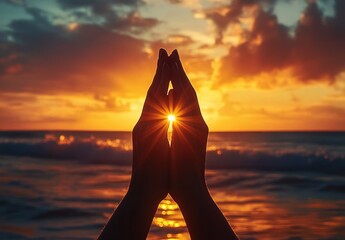 two hands pressed together in a praying gesture framing a glowing sun with bright sun rays at a vibrant sunset over the calm ocean