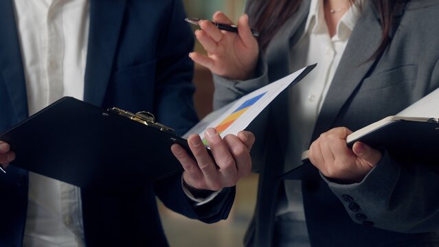 Smiling Caucasian business man boss talking Korean woman worker chart graph finance growth analyzing paperwork documents clipboard happy businessman businesswoman speaking agents strategy at office