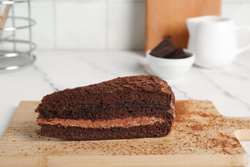 Wooden board with piece of tasty chocolate cake on marble table near beige tile wall, closeup