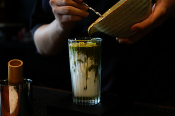 A stylish glass filled with layered matcha latte on a wooden coaster with a modern background