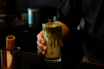 A stylish glass filled with layered matcha latte on a wooden coaster with a modern background