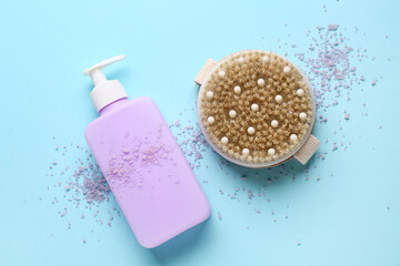 Bottle of cosmetic product, scattered sea salt and massage body brush on blue background, closeup