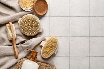 Composition with massage body brushes, glove, sea salt and bottle of cosmetic product on white tile...