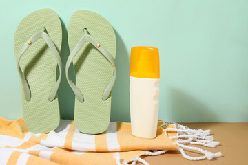 Composition with stylish beach shoes, towel and bottle of sunscreen cream on green background,...