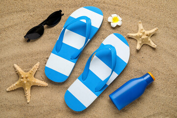 Composition with beach shoes, bottle of sunscreen cream and sunglasses on sand as background,...