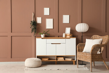 Chest of drawers, wicker armchair, pouf and floor lamp in interior of living room