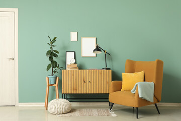 Chest of drawers, armchair and pouf near green wall in interior of living room