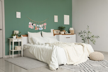 Interior of bedroom with big comfortable bed, pouf and chest of drawers near green wall