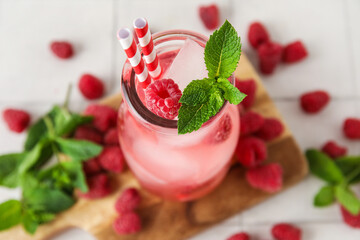 Glass of cold cocktail with raspberry on white tile background, closeup