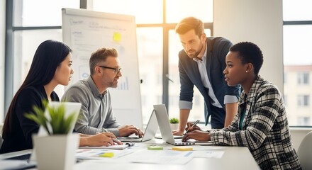 Four people in a meeting room two looking at laptops