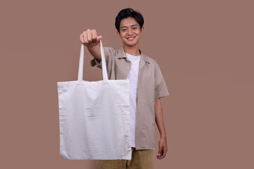 Young Man Holding White Cotton Tote Bag on Beige Background. Mockup and Zero Waste Concept.
